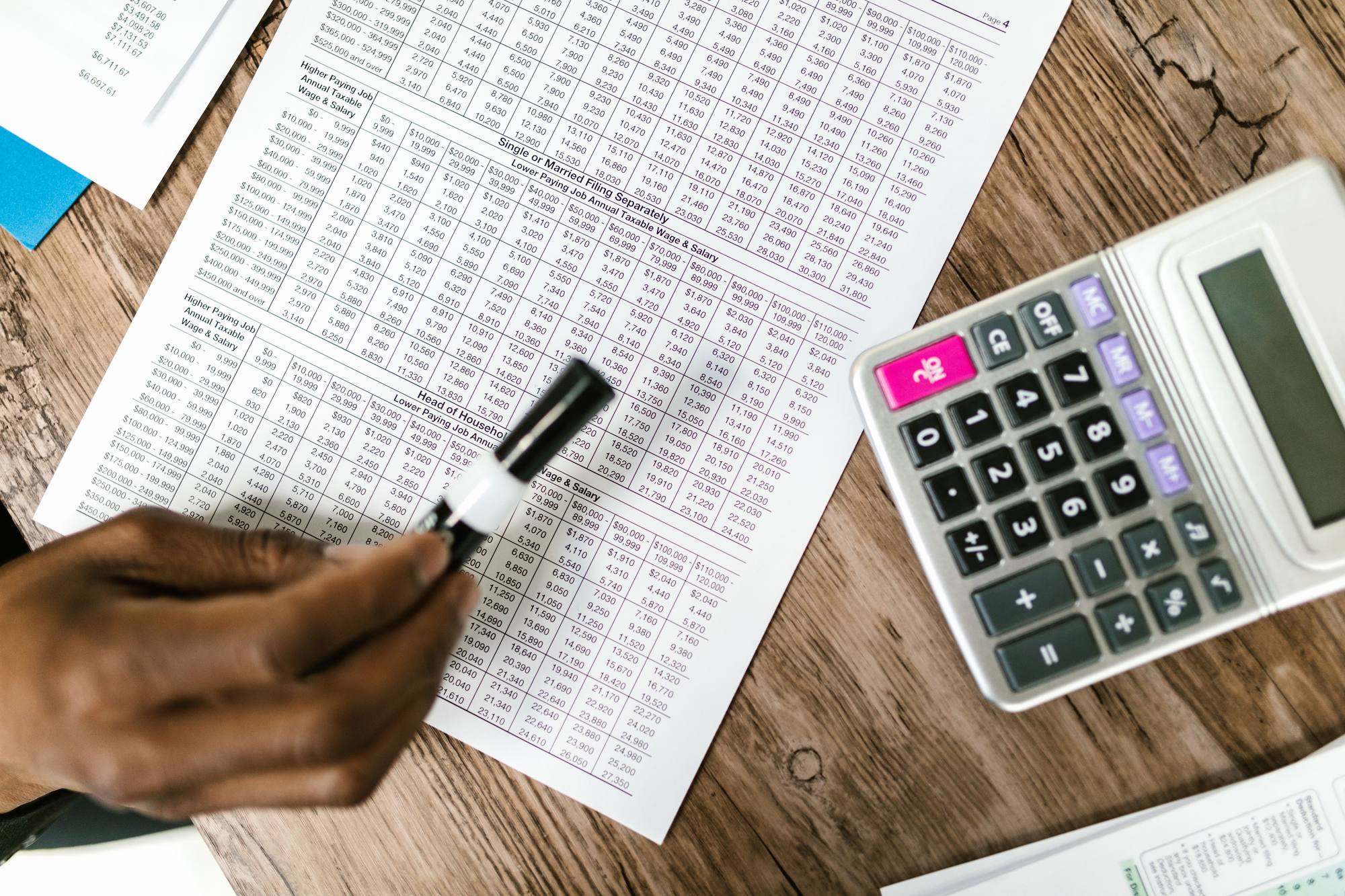 Tax tables and a calculator on a desk with a hand reviewing the figures