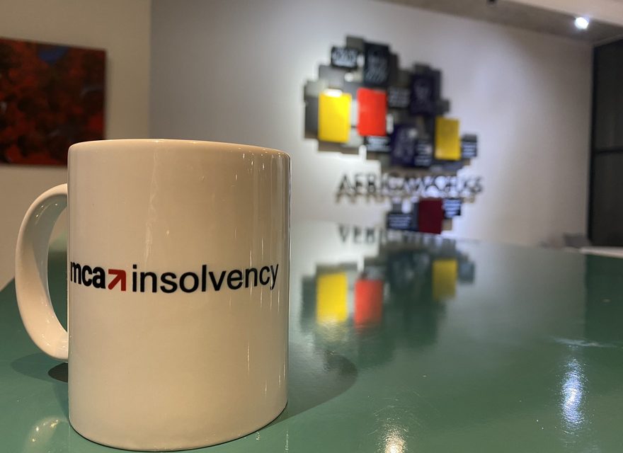 An MCA Insolvency branded mug on a table in the MCA Consulting office, with the AfricaWorks sign in the background